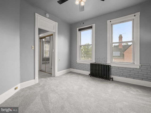 spare room with radiator heating unit, carpet flooring, a ceiling fan, and baseboards