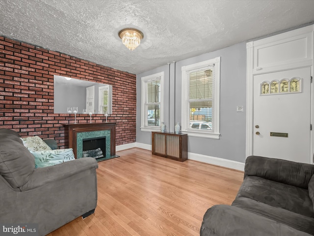 living room with light wood-style floors, a fireplace with flush hearth, a textured ceiling, brick wall, and baseboards