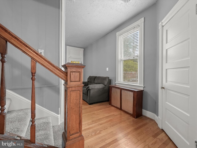 sitting room featuring a textured ceiling, light wood finished floors, stairway, and baseboards