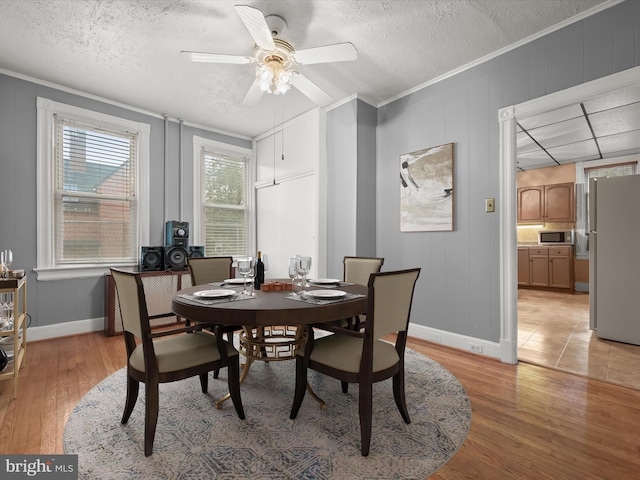 dining room with light wood-type flooring, crown molding, a textured ceiling, and baseboards