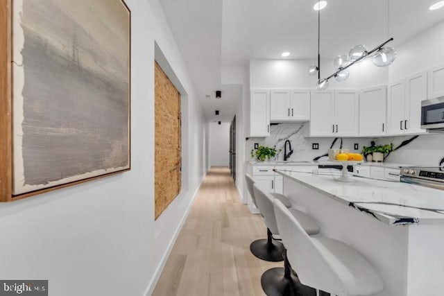 kitchen with light wood-style flooring, decorative backsplash, appliances with stainless steel finishes, white cabinets, and a sink