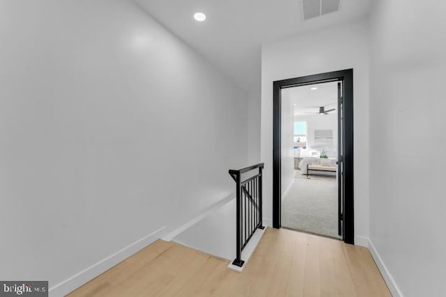 hallway featuring light wood finished floors, baseboards, visible vents, an upstairs landing, and recessed lighting