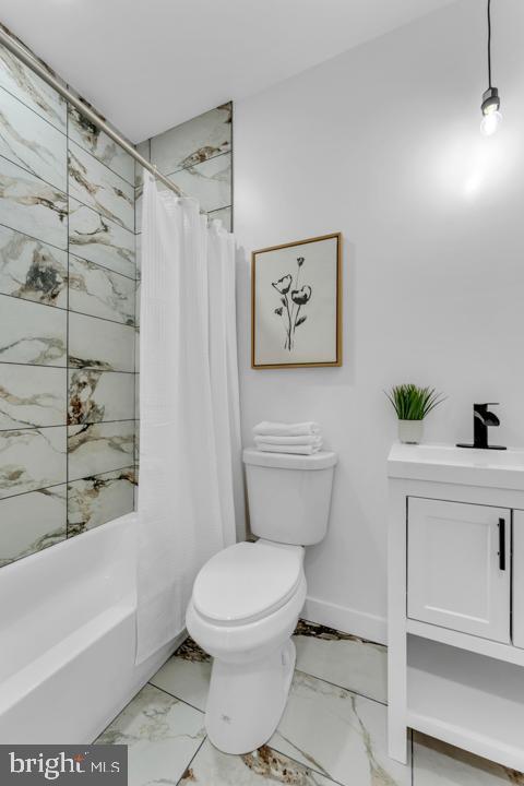 bathroom with marble finish floor, toilet, shower / bath combo with shower curtain, a sink, and baseboards