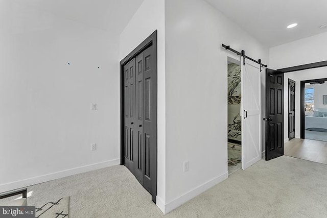 hallway with a barn door, carpet, and baseboards