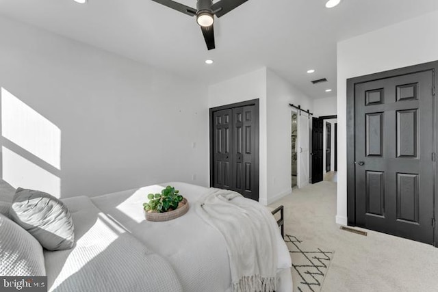 bedroom featuring recessed lighting, a closet, light colored carpet, visible vents, and a barn door