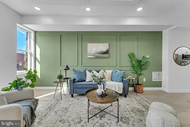 living area featuring recessed lighting, visible vents, a decorative wall, and baseboards