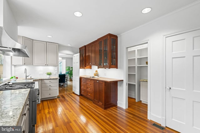 kitchen featuring extractor fan, stainless steel gas range, white fridge, wood-type flooring, and glass insert cabinets