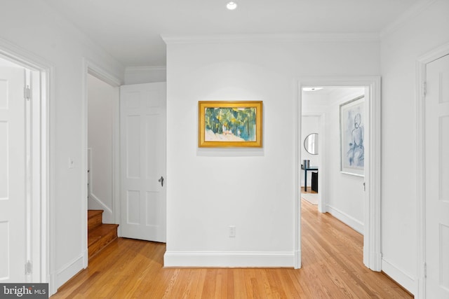 hallway featuring crown molding, light wood-style flooring, and baseboards