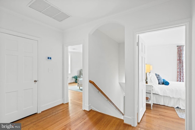 hallway with arched walkways, visible vents, light wood-style flooring, and an upstairs landing