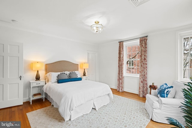 bedroom featuring ornamental molding, visible vents, baseboards, and wood finished floors