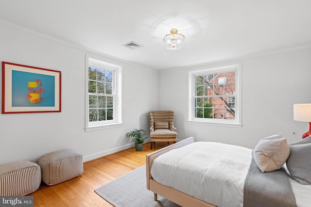 bedroom with ornamental molding, multiple windows, wood finished floors, and visible vents