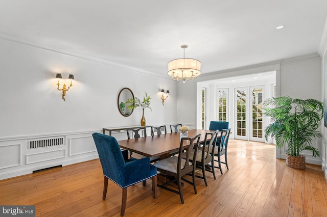 dining area with light wood finished floors, a wainscoted wall, crown molding, and an inviting chandelier