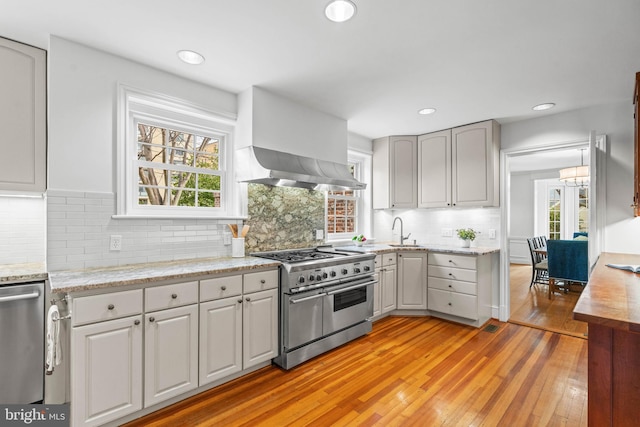 kitchen featuring recessed lighting, stainless steel appliances, wall chimney exhaust hood, light wood finished floors, and tasteful backsplash