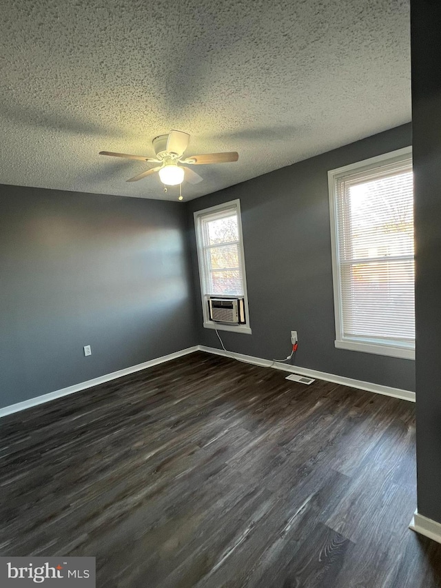 unfurnished room with a textured ceiling, cooling unit, dark wood-type flooring, visible vents, and baseboards