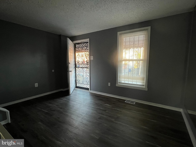 unfurnished room with a textured ceiling, dark wood-style flooring, visible vents, and baseboards