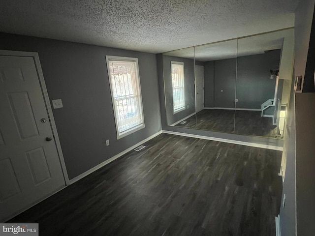 interior space with baseboards, visible vents, dark wood-type flooring, a textured ceiling, and a closet