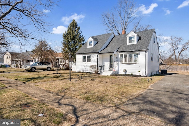 cape cod house with a shingled roof, a chimney, and a front yard