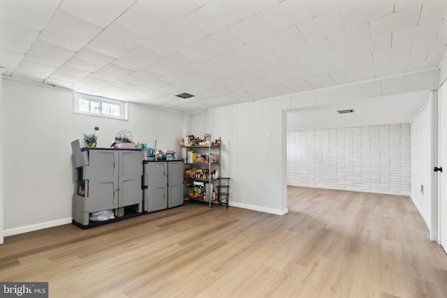 below grade area featuring light wood-style floors, brick wall, and baseboards