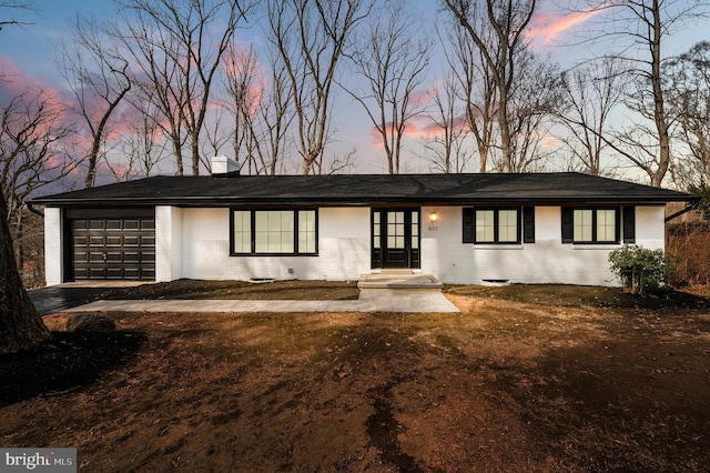 view of front of property with an attached garage, a chimney, and brick siding