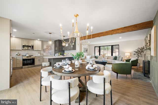 dining room featuring light wood-type flooring, a fireplace, a chandelier, and beam ceiling