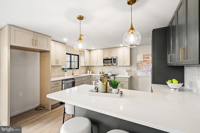 kitchen featuring light wood finished floors, tasteful backsplash, a peninsula, stainless steel appliances, and a sink