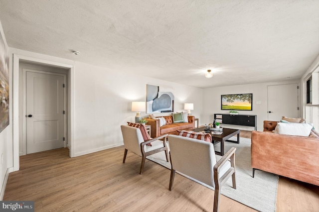 living area featuring a textured ceiling, light wood-type flooring, and baseboards