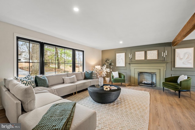 living room featuring recessed lighting, a fireplace, a decorative wall, and light wood finished floors