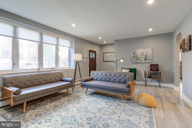 living room featuring arched walkways, recessed lighting, light wood finished floors, and baseboards