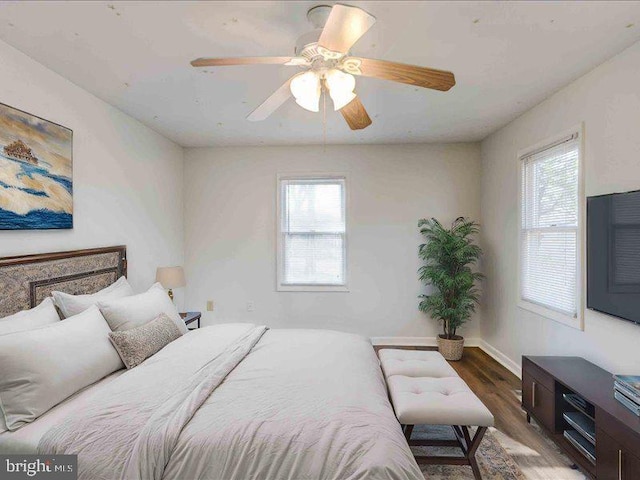 bedroom featuring multiple windows, baseboards, a ceiling fan, and wood finished floors