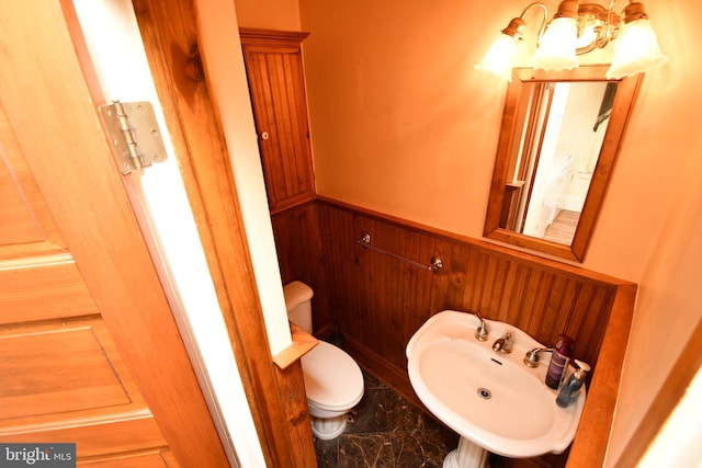 half bathroom featuring a sink, a wainscoted wall, toilet, a chandelier, and wooden walls