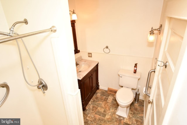 bathroom with stone finish floors, a wainscoted wall, toilet, and vanity