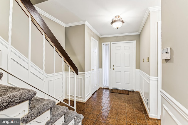 foyer entrance with a decorative wall, stairway, ornamental molding, and wainscoting