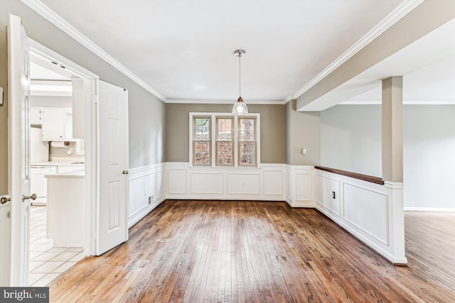 unfurnished dining area featuring a wainscoted wall, light wood-type flooring, and crown molding