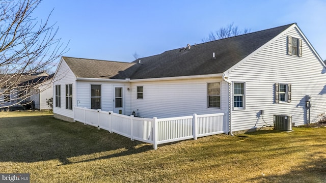 rear view of property with roof with shingles, a lawn, cooling unit, and fence