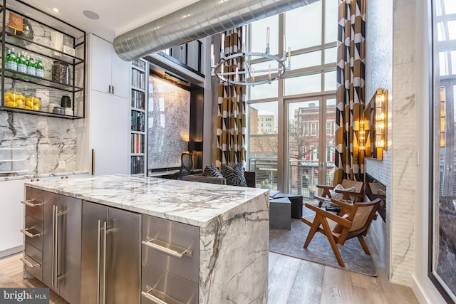 kitchen with plenty of natural light, light wood-type flooring, decorative backsplash, and light stone countertops