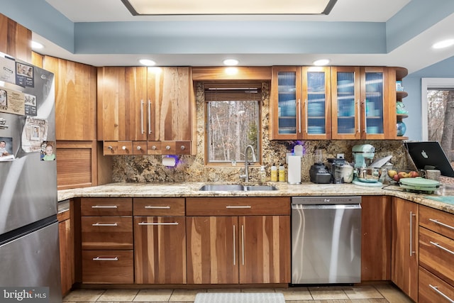 kitchen featuring decorative backsplash, brown cabinetry, appliances with stainless steel finishes, light stone countertops, and a sink