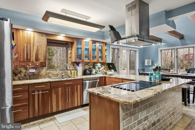 kitchen featuring island range hood, stainless steel appliances, a peninsula, a sink, and decorative backsplash