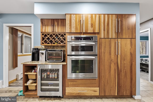 kitchen with a toaster, double oven, brown cabinetry, light stone countertops, and beverage cooler