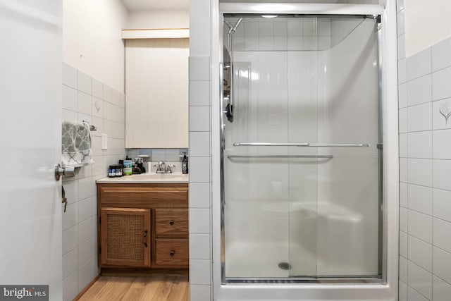 bathroom with wood finished floors, a shower stall, and tile walls