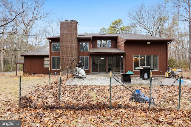 back of property with roof with shingles, a chimney, a patio area, and a sunroom