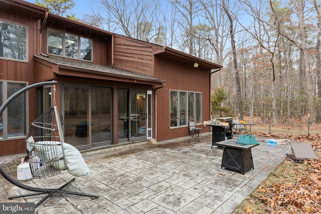 back of property featuring a shingled roof, a fire pit, and a patio