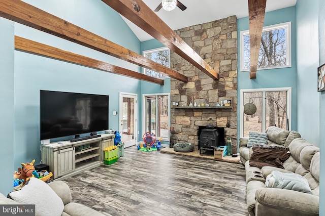 living room with a ceiling fan, a towering ceiling, wood finished floors, a wood stove, and beam ceiling