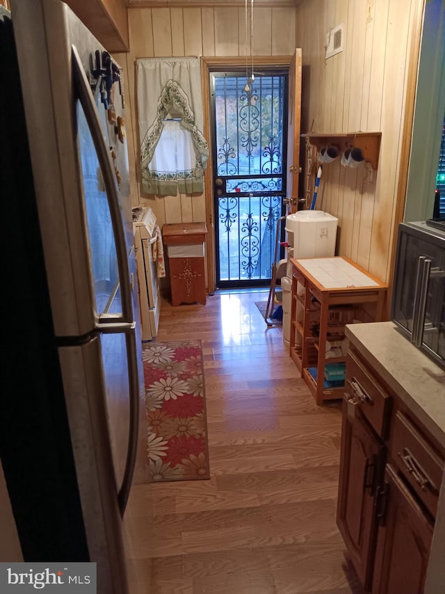 kitchen featuring light wood finished floors, wooden walls, light countertops, freestanding refrigerator, and washer / clothes dryer