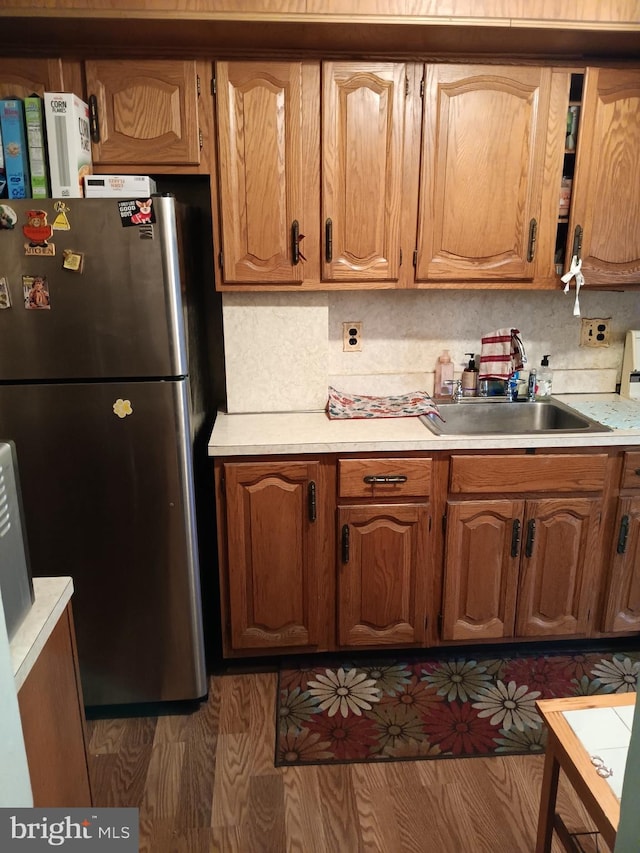 kitchen featuring decorative backsplash, light countertops, freestanding refrigerator, and a sink