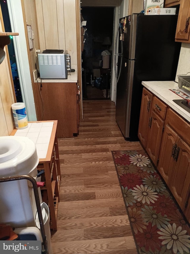 kitchen featuring brown cabinets, wood finished floors, freestanding refrigerator, and light countertops