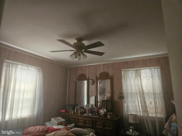 bedroom with ceiling fan, wooden walls, and ornamental molding