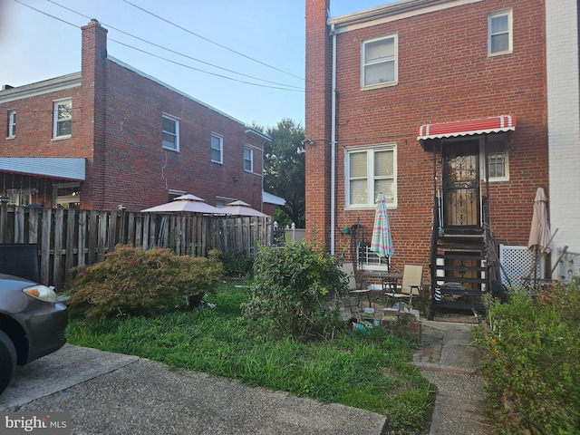 rear view of house featuring entry steps, fence, and brick siding