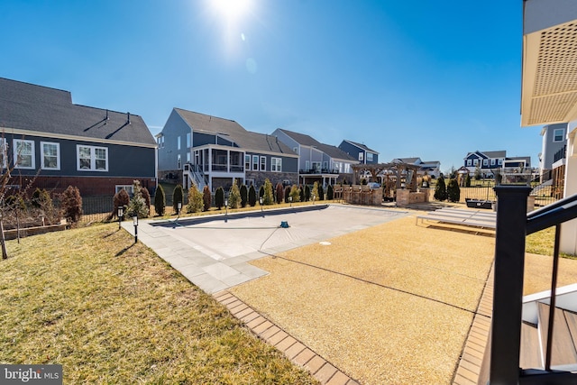 view of basketball court featuring a residential view, fence, and a lawn