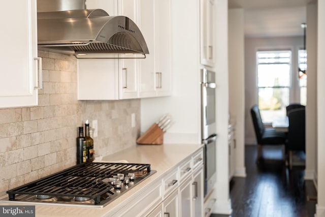 kitchen featuring appliances with stainless steel finishes, light countertops, white cabinetry, backsplash, and exhaust hood