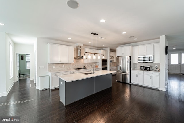 kitchen with wall chimney exhaust hood, appliances with stainless steel finishes, light countertops, white cabinetry, and a sink